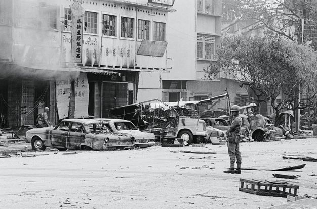 Black and white photograph. Two uniformed soldiers stand on a street lined with burned-out cars and buildings.